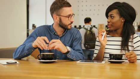 young caucasian man in glasses drinking coffee with african american woman in a modern coffee shop