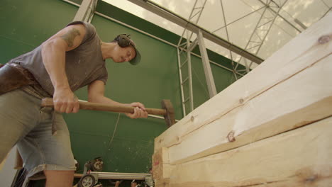 carpenter strikes big wooden log into place with sledge hammer, log cabin build