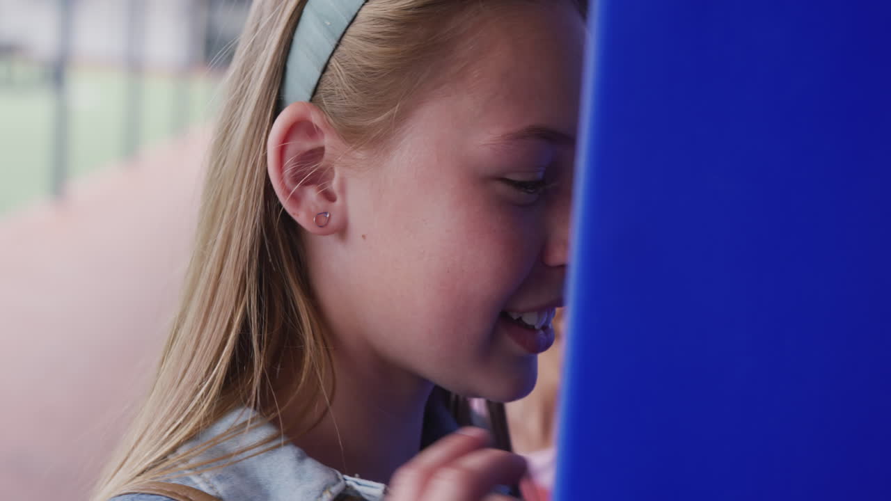 Video of two diverse, happy schoolgirls talking by lockers in school corridor, copy space