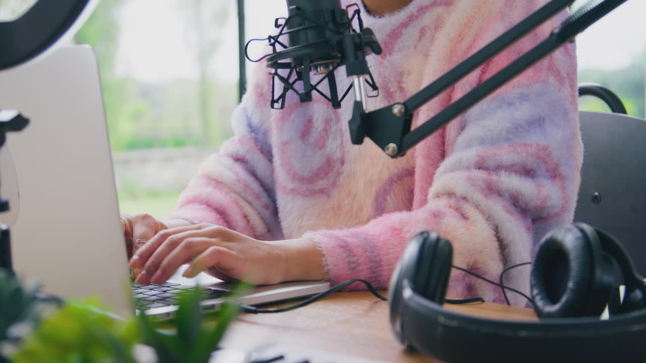 Close Up Of Female Vlogger Typing On Laptop With Headphones And  Microphone In Foreground