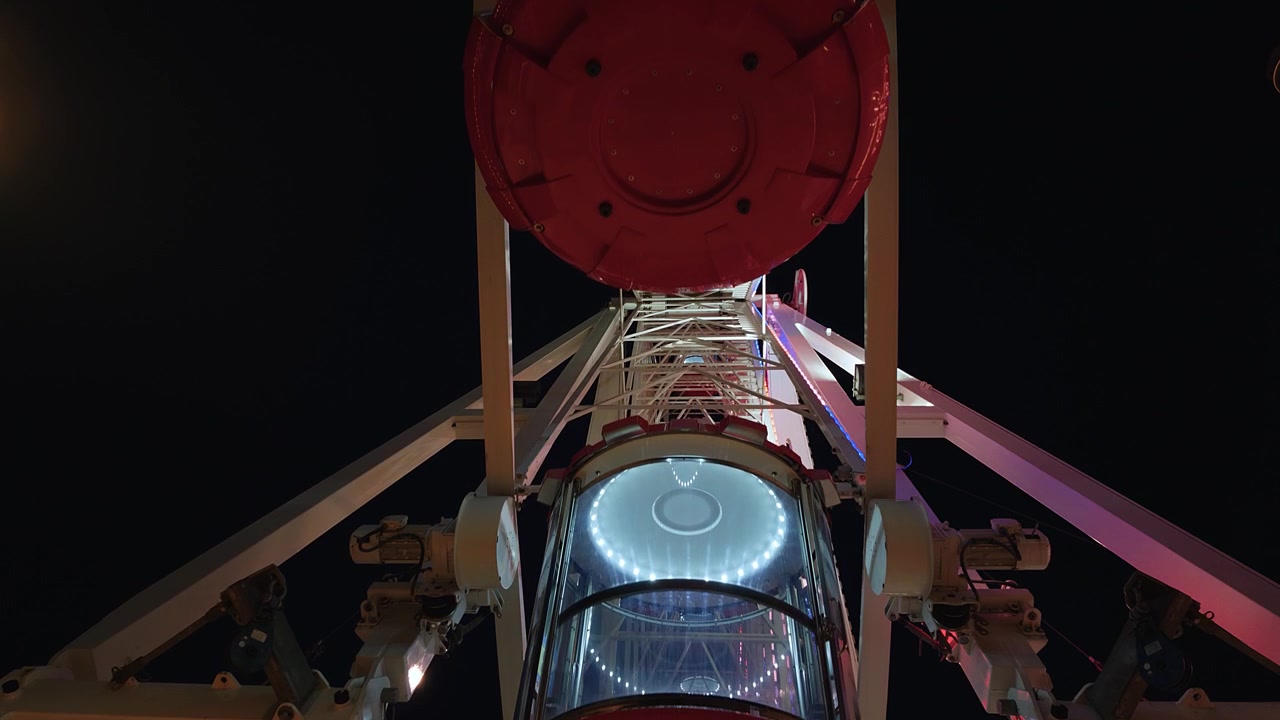 A dramatic low angle shot of illuminated red ferris wheel cabins rotating against a dark night sky during the Electric Summer event in London.