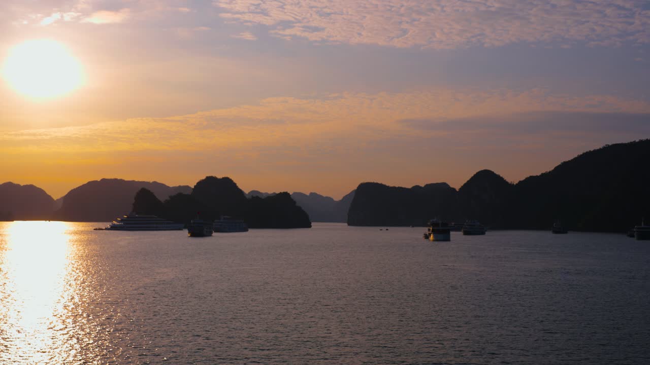 Sunrise over Ha Long Bay with silhouetted many cruise ships anchored, Vietnam - aerial pan