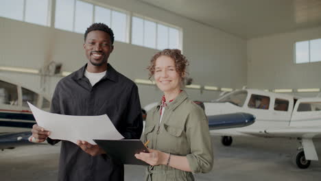 portrait of two diverse ground technicians smiling at camera in aviation hangar