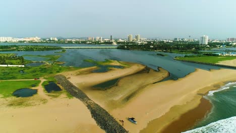 Drone-video-of-a-beach-with-waves-crashing-with-a-city-skyline-dotting-high-rise-buildings-in-the-backdrop