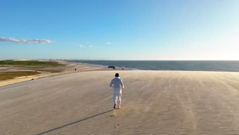 man dressed in soft clothing running through the dunes of jericoacoara