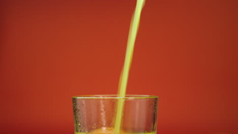 close-up slow motion footage of fresh orange juice pouring and spilling in a highball glass, isolated on an orange background