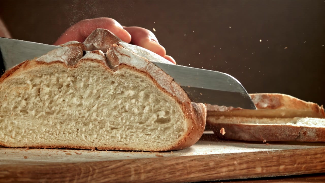 Primo piano di una persona che affetta pane fresco su un tagliere di legno al rallentatore.