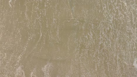 foamy ocean waves washing sand of tropical beach - top down view