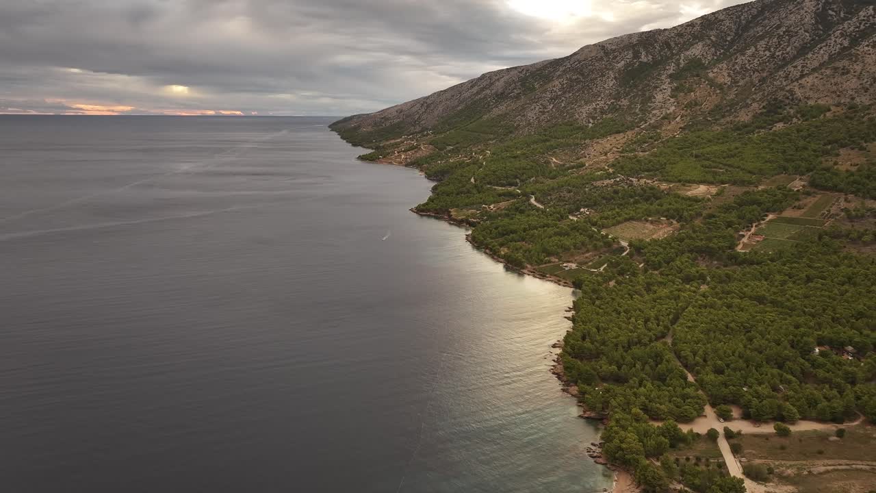 Fly over the lush forests along the Adriatic coast on Brač Island. This aerial footage captures the natural beauty of the island, where vibrant greenery meets the crystal-clear waters of the sea