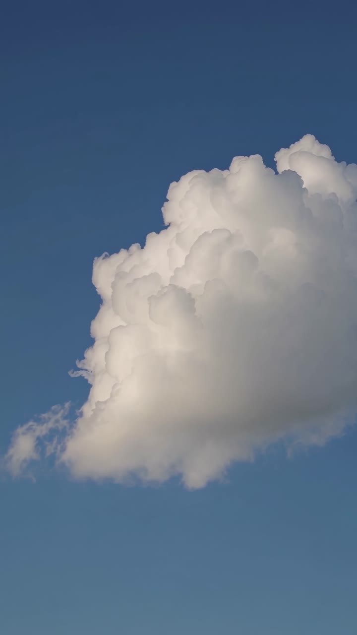 A serene video captures a fluffy white cloud against a clear blue sky, shot from a low angle