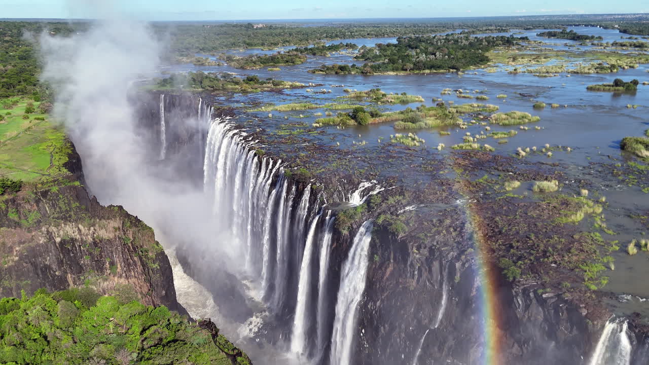 Aerial view of Victoria Falls with powerful waterfall plunging into gorge, mist rising above lush green forest, dramatic natural wonder and iconic travel destination in Africa