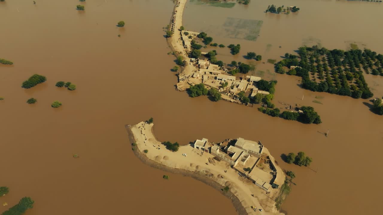 High orbiting drone looks down on vast submerged fields, treetops, and waterlogged residential complexes under intense sun