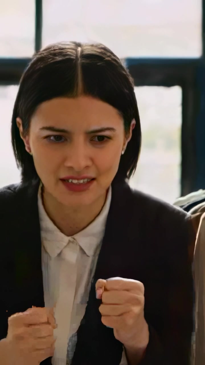 Video verticale: Donna in blazer che si appoggia in un ufficio vicino alla finestra, afferrando la manica e cercando conforto dopo una discussione.