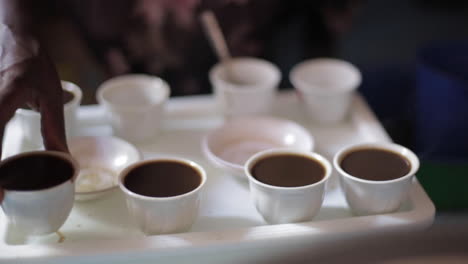 coffee is served by african woman, many small cups, close up hands