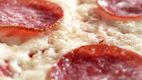 queso derretido y salchichas de salami marrones en la parte superior de la pizza de pepperoni giratoria, macro y cámara lenta