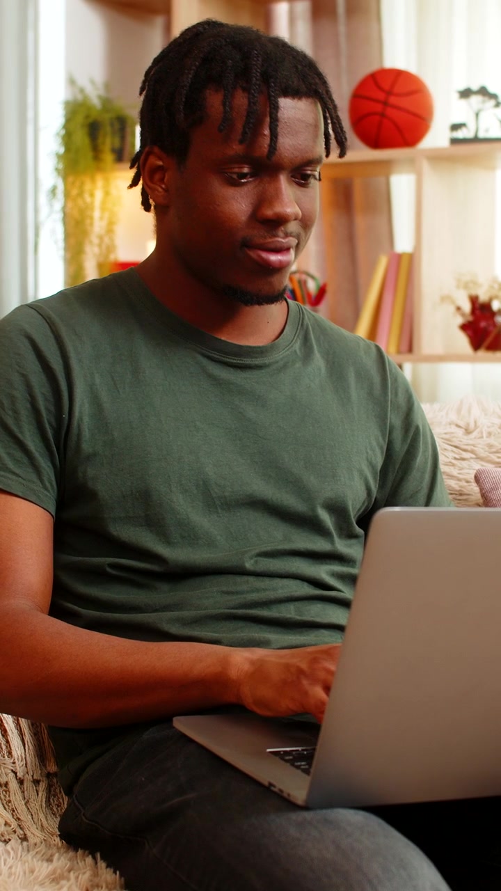 African american young man on home sofa opening laptop typing email for remote work in living room
