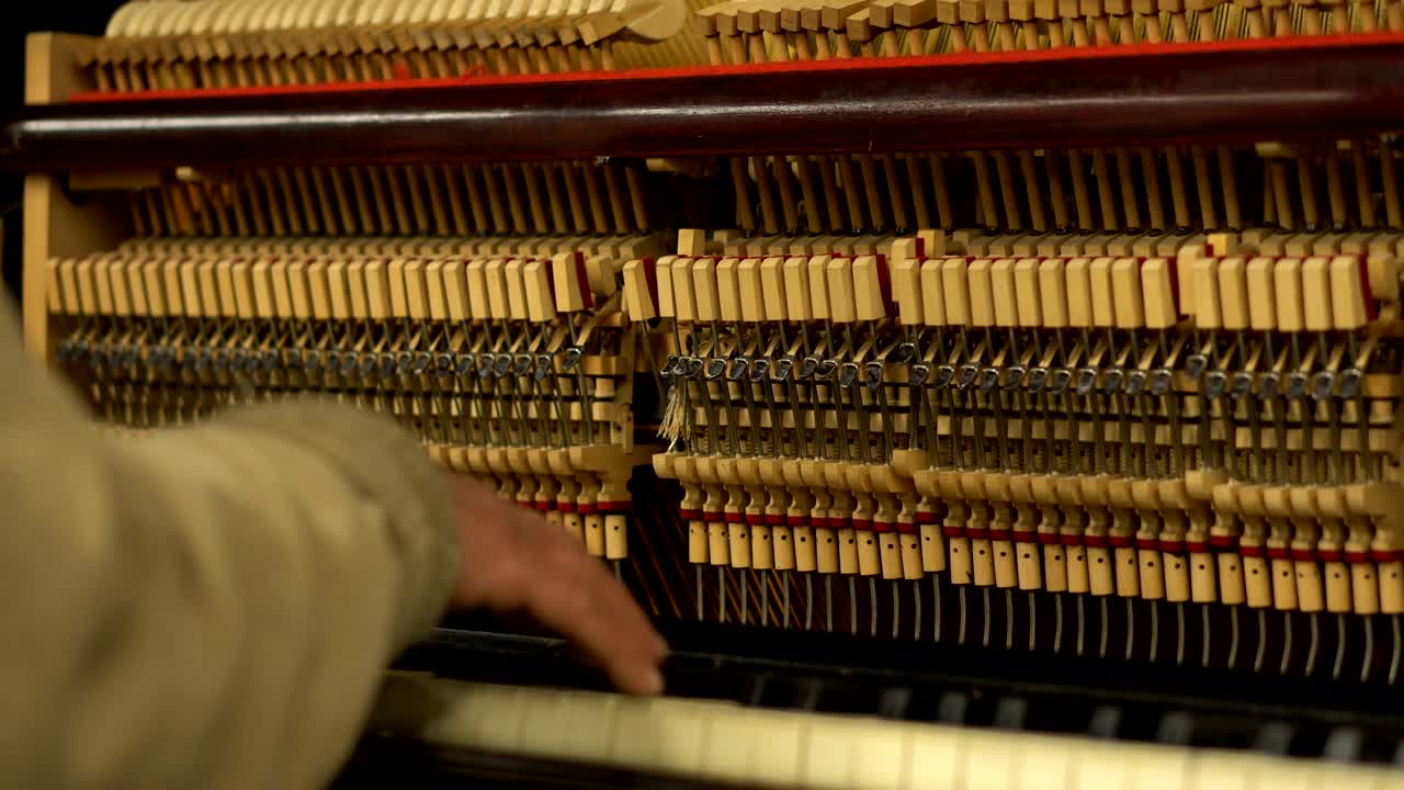 Mani di un anziano in metropolitana che suona il pianoforte con meccanismo aperto di corde e martelletti