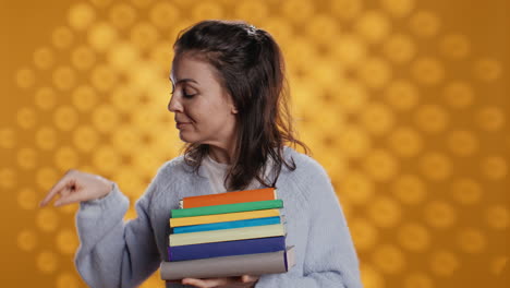 Portrait-of-smiling-woman-holding-pile-of-books-pointing-to-empty-copy-spaces