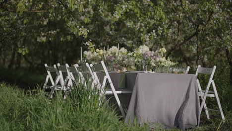 dinner-table-with-flower-decoration-in-blooming-garden-in-spring-day-romantic-open-air-event-and-catering