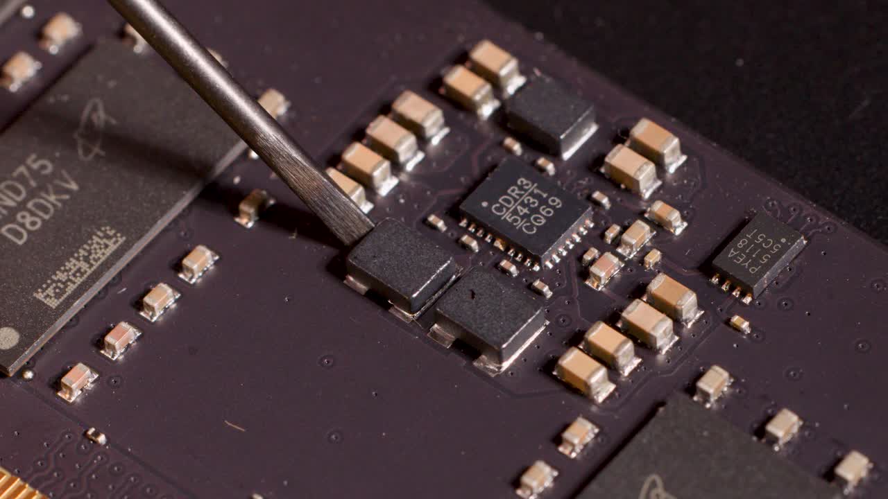 Metal tool points at microchip on circuit board under bright lighting, macro close-up view