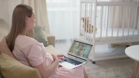 pregnant woman sitting on sofa and using a laptop in online consulation with a doctor