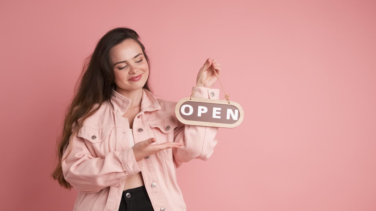 Smiling woman with open sign inviting in pink studio