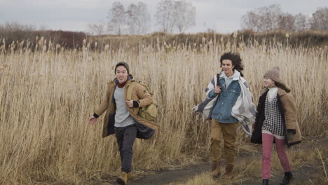 Two-Teenage-Boy-And-Girl-And-Teenager-Boy-With-Long-Hair-Wearing-Winter-Clothes-Walking-In-A-Wheat-Field-On-A-Cloudy-Day