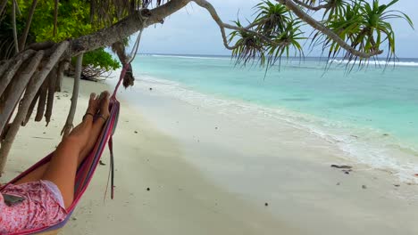 static shot of young tanned girl rocking peacefully in a hammock on a palm tree on a tropical beach paradise in maldives