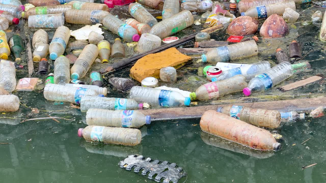Bottiglie di plastica scartate e detriti galleggiano in acqua verde torbida all'interno di un canale di cemento.