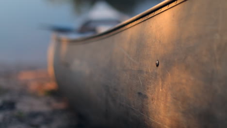 used and scratched metal canoe on side of river during sunset