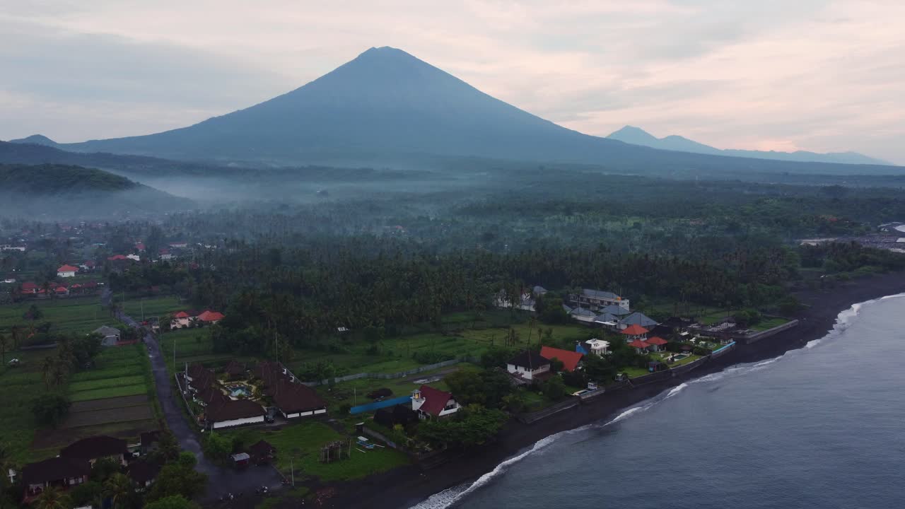 Filmato aereo di un villaggio di pescatori all'alba con la nebbia che avvolge la giungla di palme e il vulcano attivo Monte Agung.