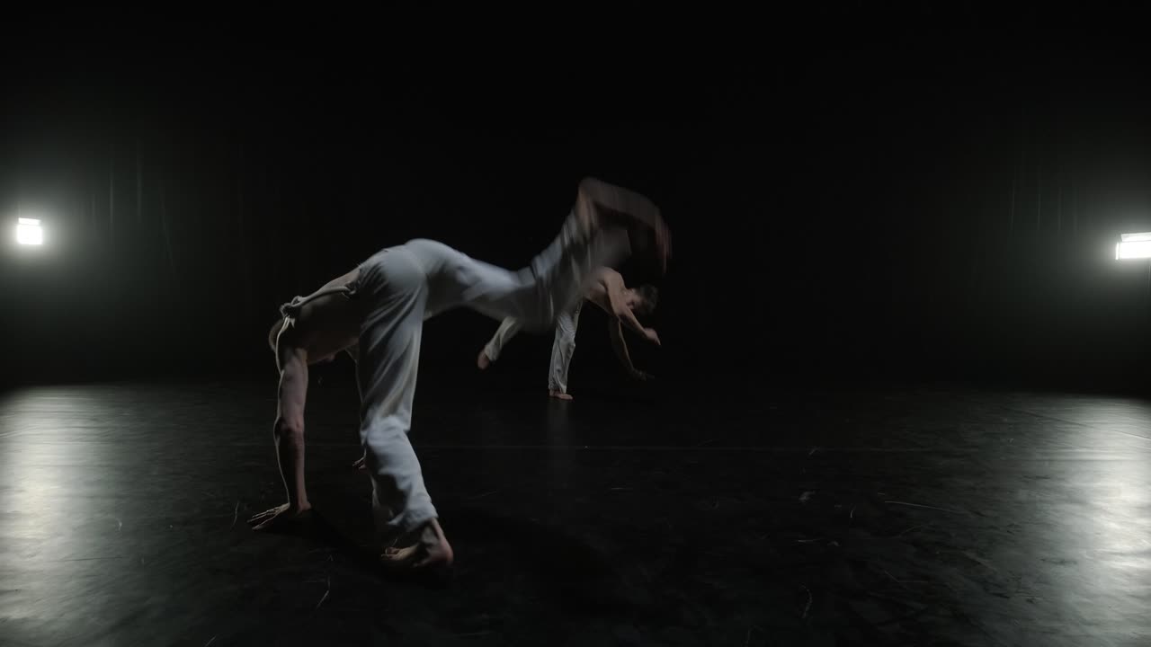 un grupo de bailarines profesionales están practicando capoeira en la oscuridad contra un foco de luz en un fondo negro de estudio. arte marcial afro-brasileño que combina elementos de la danza.