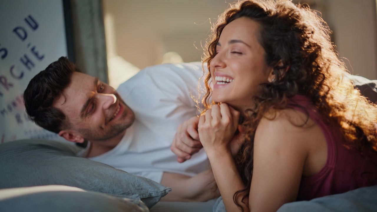 Casal apaixonado deitado na cama em uma manhã ensolarada. Namorado tocando o cabelo da mulher com ternura.
