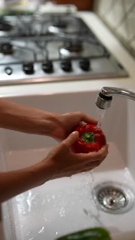 washing a red bell pepper in a kitchen sink