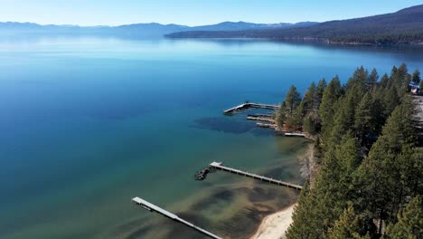 Drone-flyover-of-the-North-shore-of-Lake-Tahoe,-shoreline-lined-with-trees-and-empty-boat-docks