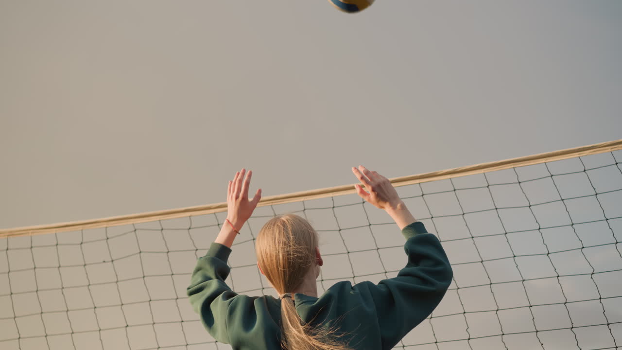 볼리볼 선수가 망에 대한 공을 차단하기 위해 손을 는 클로즈업, 빛으로 따뜻한 빛을 만들어, 뒷면은 흐릿한 하늘과 부드러운 자연 빛으로 집중된 운동 운동을 포착합니다.