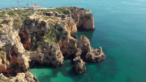 impresionantes escarpas que rodean el faro de ponta da piedade, lagos algarve, portugal - toma de órbita panorámica aérea amplia