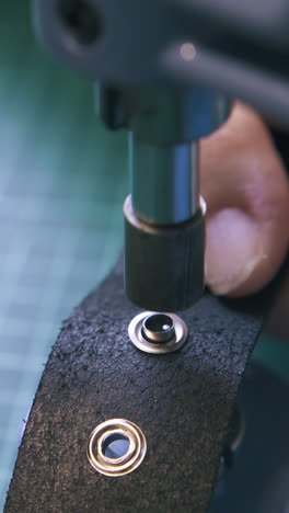 cu: experienced tailor fixes silver eyelets on black leather belt with press machine on green cutting board closeup