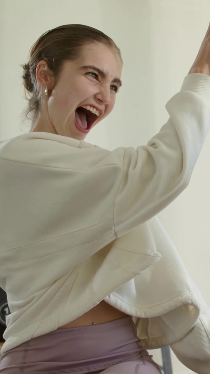 Vertical video: Laughing woman in hoodie turning to friend entering gym, hugging near kettlebells