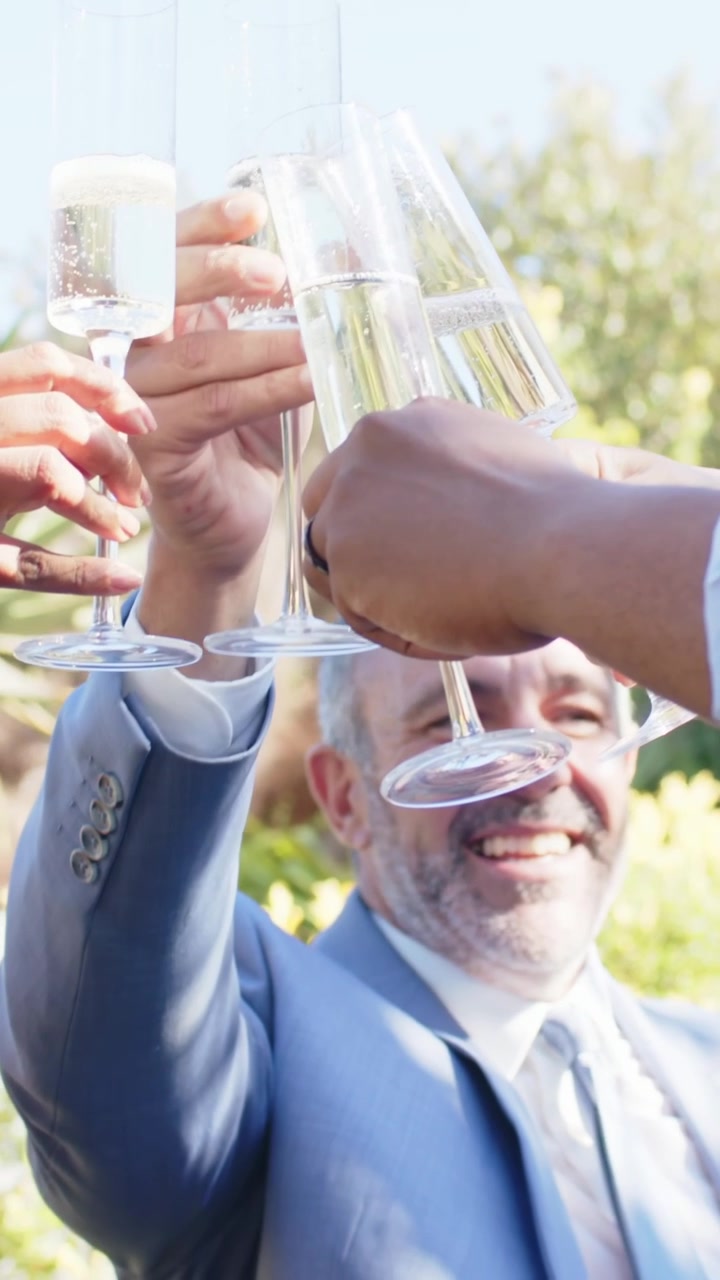Vertical video: Rising flutes starting toast, man in light blue suit leading celebration in garden