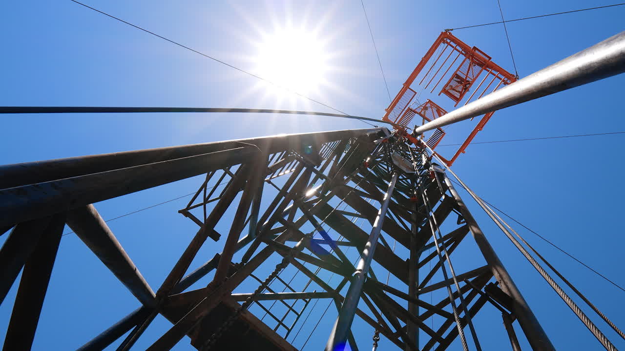 Standing at the foot of the metal tower used for drilling oil or gas. Low angle view on the derrick at resource producing site.