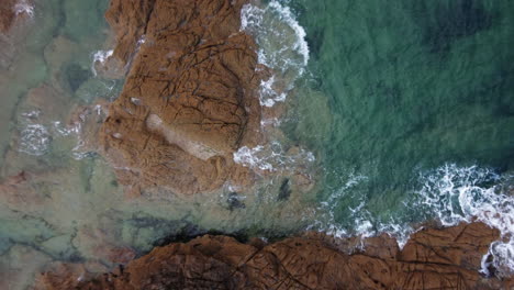 Aerial-top-down-descending-over-waves-crashing-on-rocky-coast-of-Saint-Malo-in-Brittany,-France