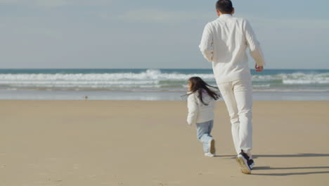 japanese father and little daughter running and playing game of tag on the beach