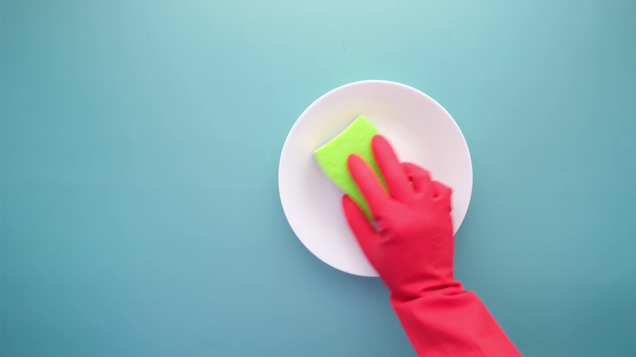 Cleaning a Plate with a Green Sponge and Red Gloves