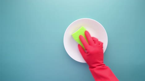 limpiando un plato con una esponja verde y guantes rojos