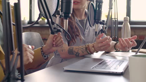 mãos de homem e mãos de mulher gesticulando na mesa enquanto gravam um podcast