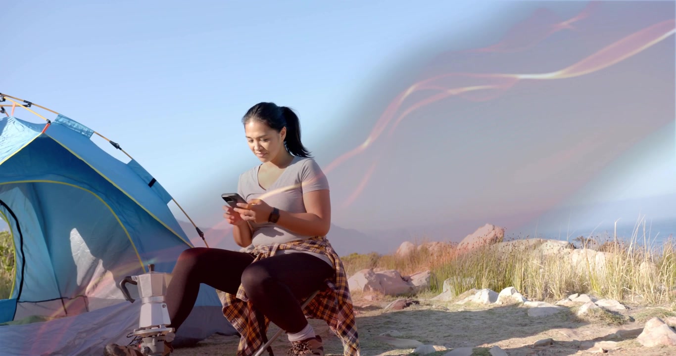 Donna all'aperto che controlla le notifiche dello smartphone dopo aver montato la tenda in un campo sabbioso con un cielo vorticoso.