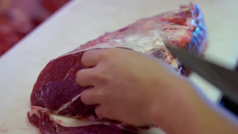 Primer-Plano-De-Las-Manos-De-Un-Carnicero-Con-Un-Cuchillo-Cortando-Carne-Roja-Sobre-Una-Pizarra-Blanca