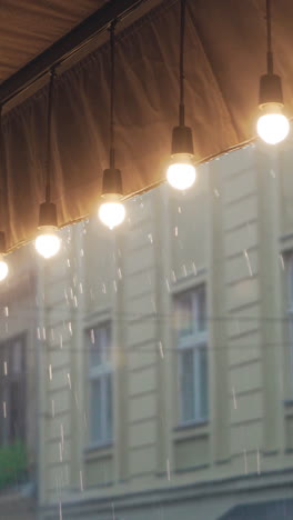 view on a row of burning light bulbs from the roof of a restaurant on the background of raindrops from the street. it's raining vertical video