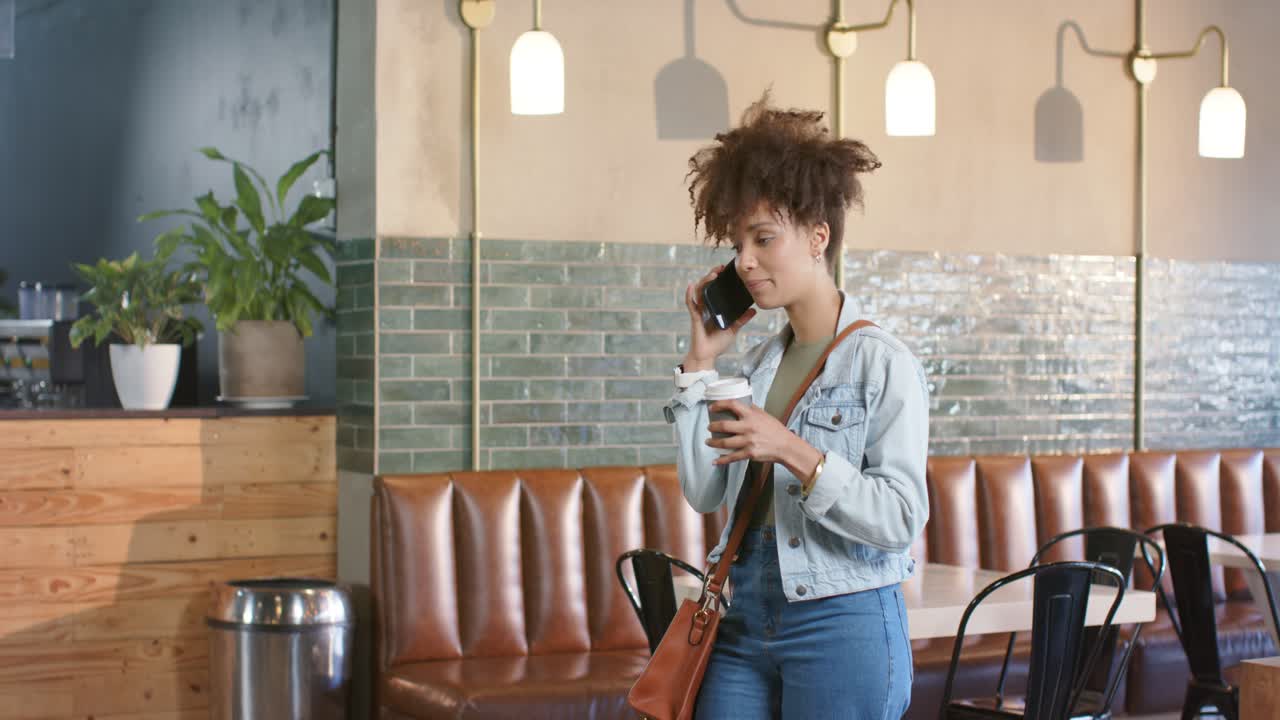 Donna adulta con giacca di jeans riceve una chiamata, tiene lo smartphone e beve da un bicchiere di carta in caffetteria